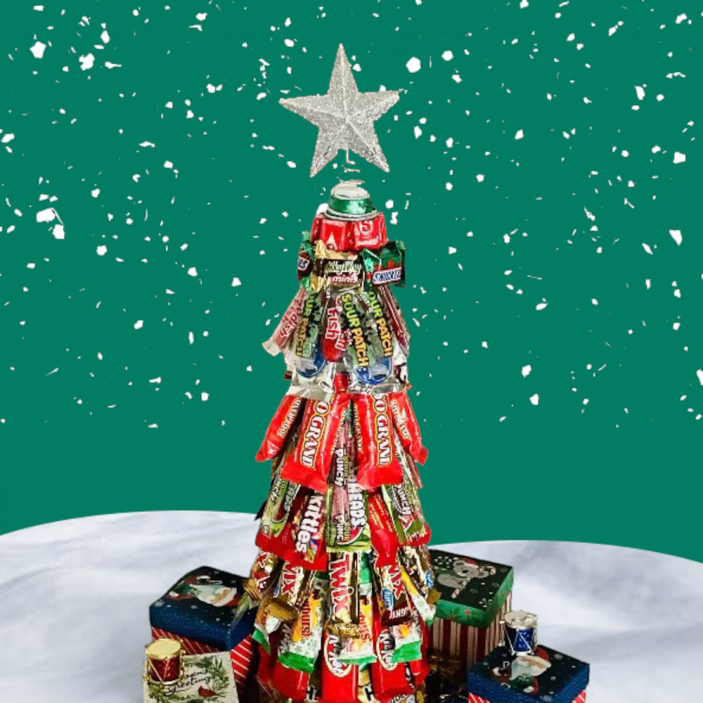 CandyCakeExplosion Christmas tree made of assorted candy bars and chocolates topped with a silver star on a snowy base.