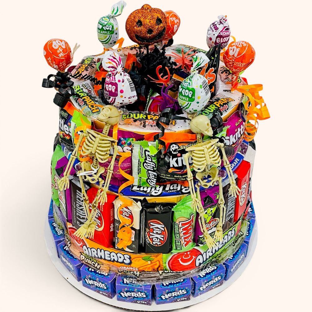 CandyCakeExplosion large Halloween candy cake featuring chocolate bars, fruity treats, skeleton figures, and a pumpkin topper.