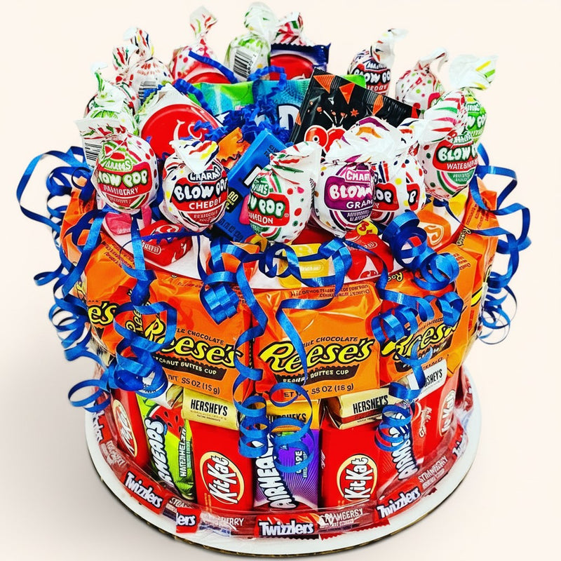 CandyCakeExplosion medium peanut butter candy cake decorated with Reese's, KitKats, Blow Pops, and blue ribbons.
