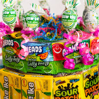 CandyCakeExplosion medium sour candy cake featuring Charms Blow Pops, Laffy Taffy, and Sour Patch Kids with pink ribbon